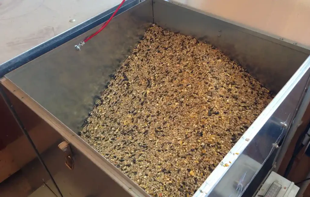 Nahaufnahme einer hellen Futtermischung (Kraftfutter) für Pferde: Man sieht eine grobe Struktur mit hellbraunen Pellets, goldgelben Getreideflocken und kleinen, dunkleren Körnchen vermischt. Die einzelnen Komponenten sind deutlich zu erkennen, das Licht hebt die Textur hervor.